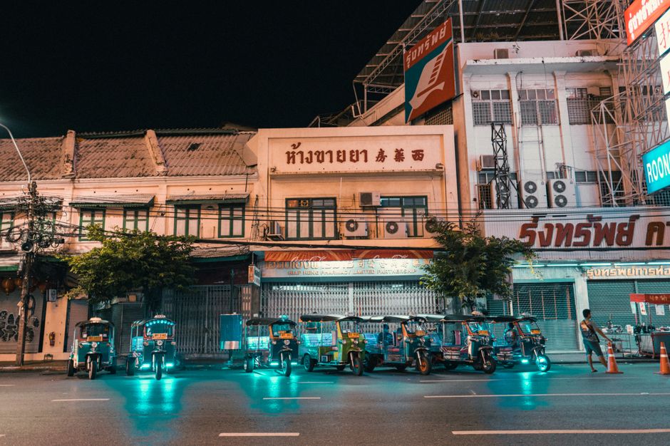 Vibrant night scene featuring electric tuk-tuks parked in front of lit-up city buildings.
