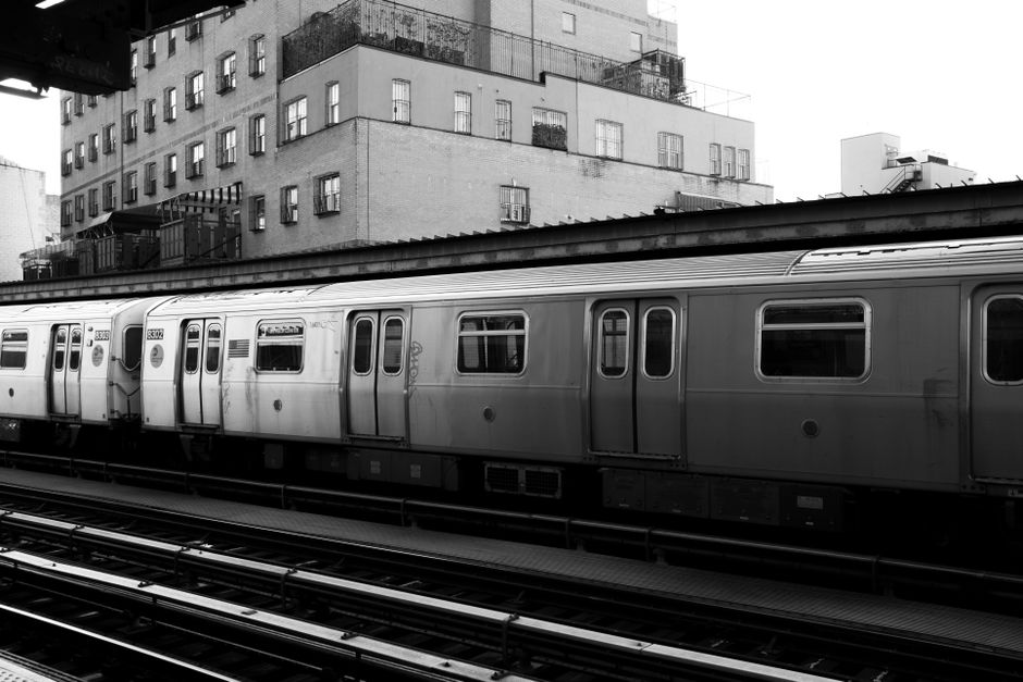 Black and white photo of a subway train passing by urban buildings, capturing city life.