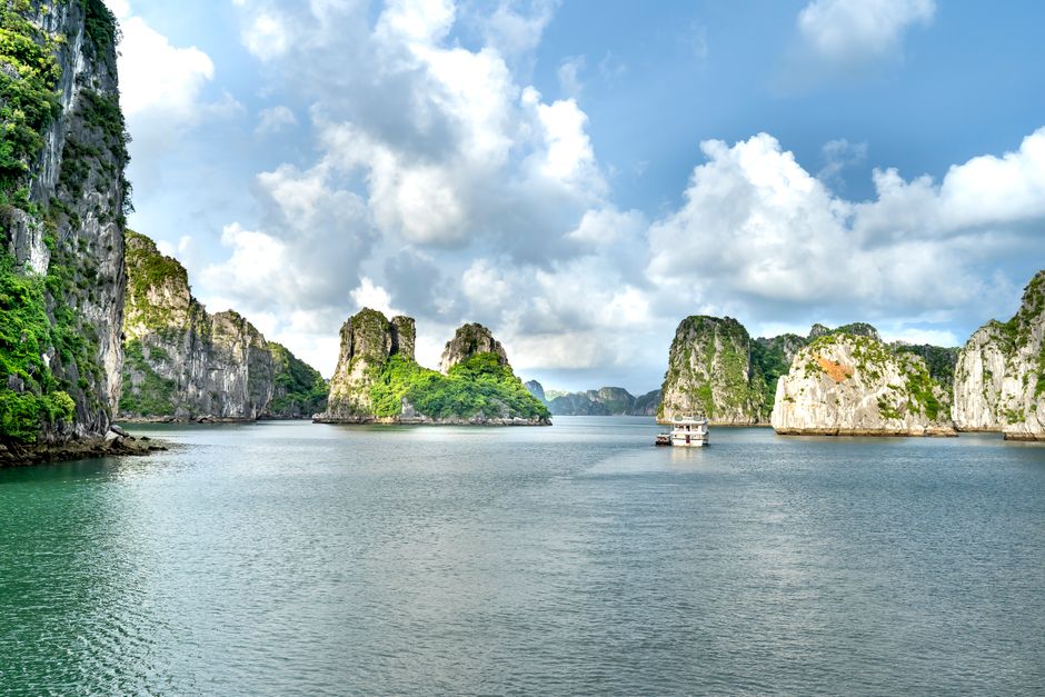 Breathtaking view of Ha Long Bay's limestone cliffs with green foliage under a bright sky.