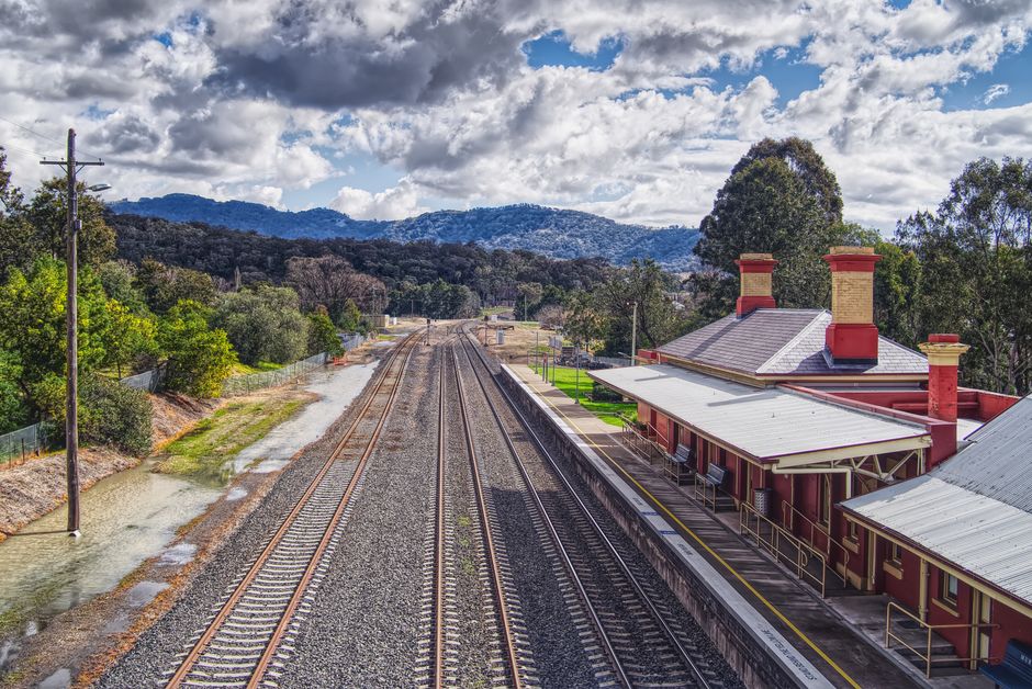 Charming railway station amidst mountains and lush forests under dramatic skies.