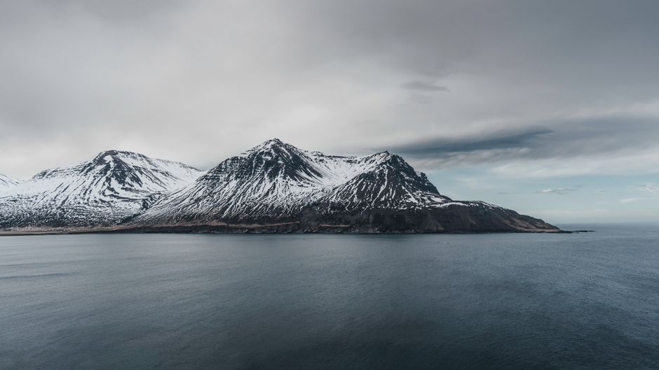 A breathtaking view of snow-covered mountains meeting the vast ocean in Iceland.
