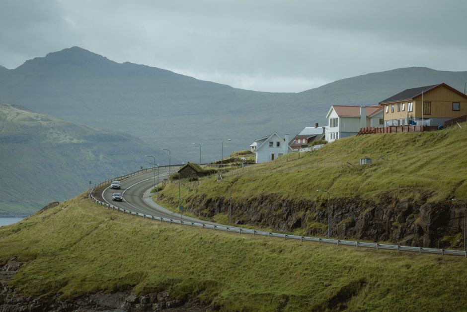 A winding road passes through a picturesque village set against mountain views.
