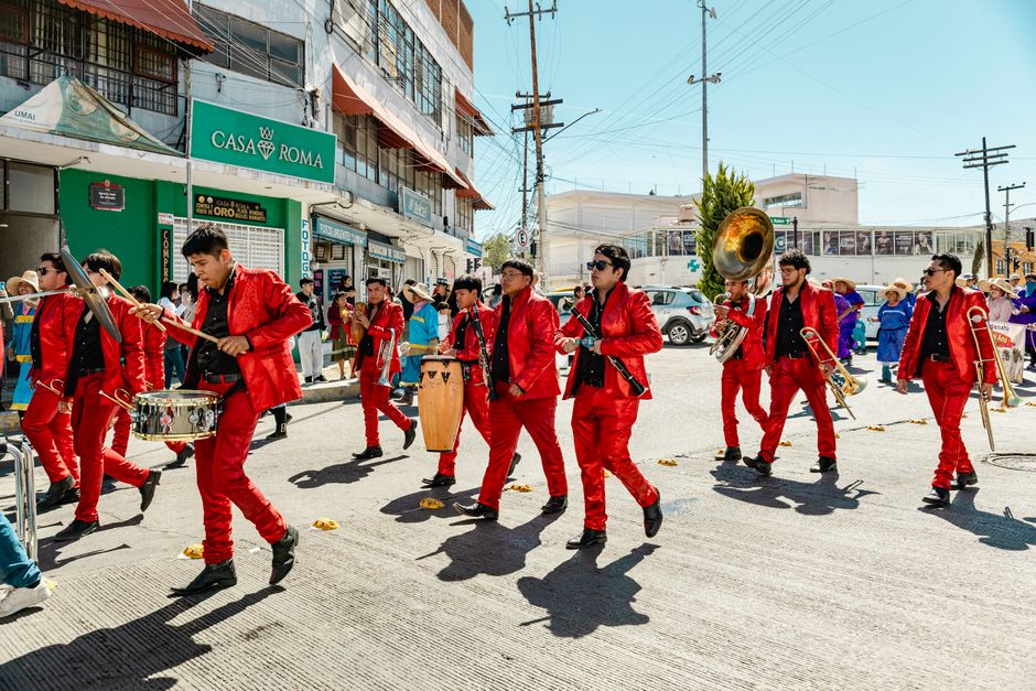 Musicians in vibrant red suits perform in a lively street parade in Pachuca, Mexico.