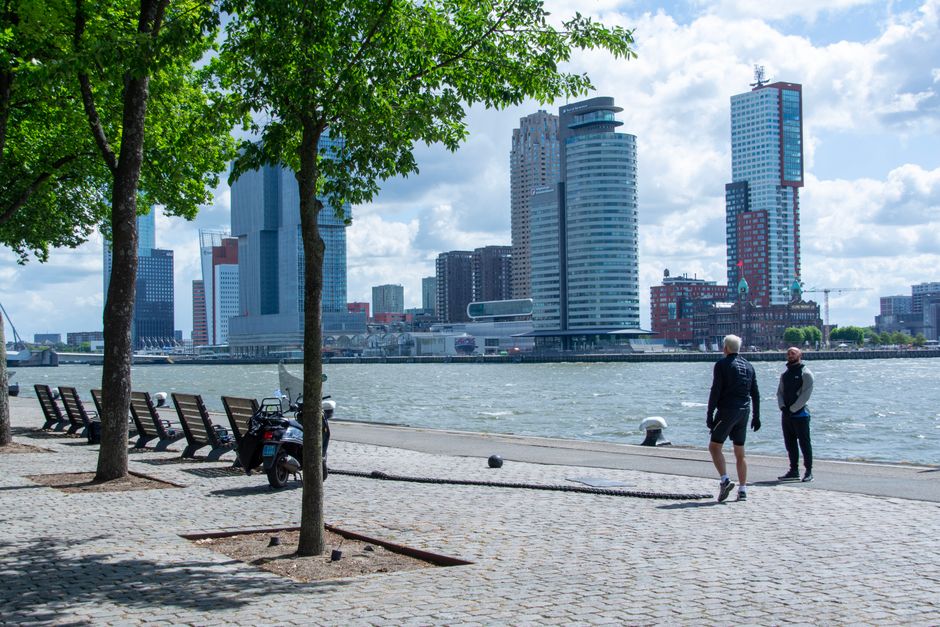 People enjoying a walk by the river with Rotterdam city skyline in the background.