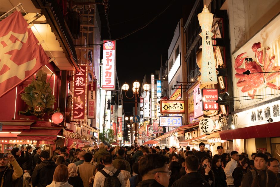 Vibrant night scene capturing a bustling crowd and bright neon signs on Dotonbori Street, Osaka.