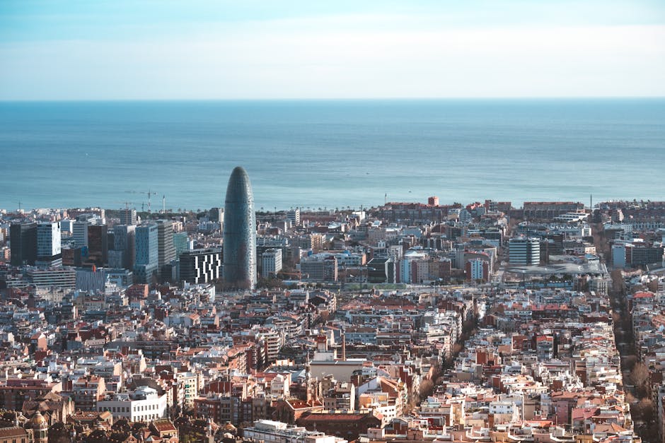 Aerial view of Barcelona cityscape featuring Torre Glòries with the Mediterranean Sea in the background.