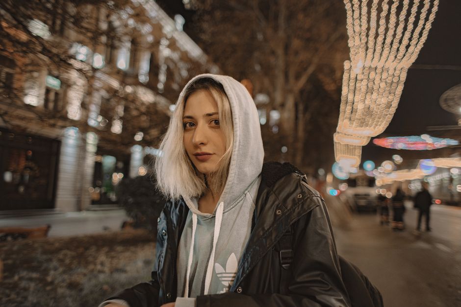 Stylish woman in urban setting with lights at night wearing a leather jacket and hoodie.