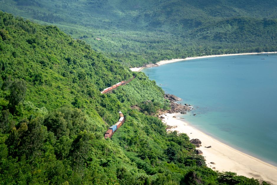 Train going through lush green forest with green trees growing on mountain near sandy shor
