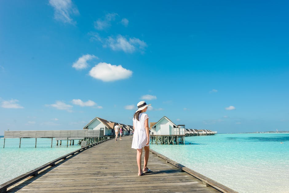 Woman in white dress on a wooden dock over turquoise water under a blue sky.