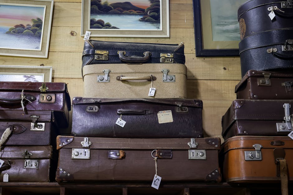 A collection of vintage suitcases stacked in an antique store with framed art on the wall.